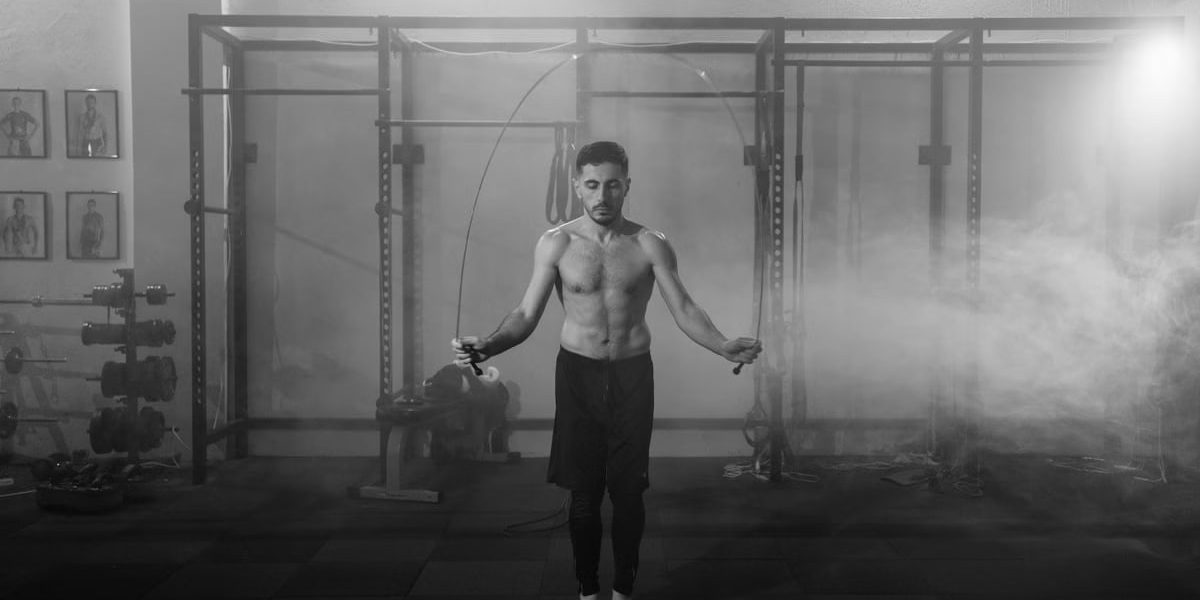 Muscular man doing a jump rope workout in an industrial gym setting with dramatic smoke around.