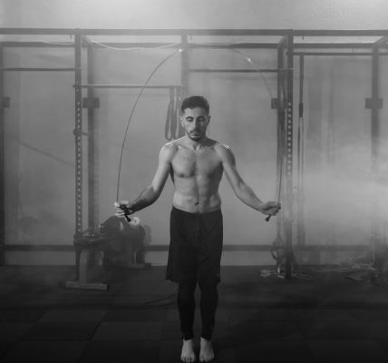 Muscular man doing a jump rope workout in an industrial gym setting with dramatic smoke around.