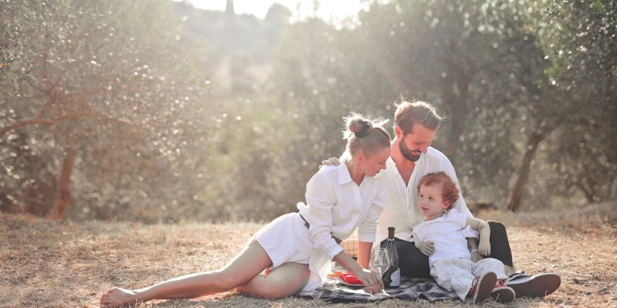 Happy family enjoying a picnic in an olive grove under the sun. Perfect for lifestyle and outdoor themes.